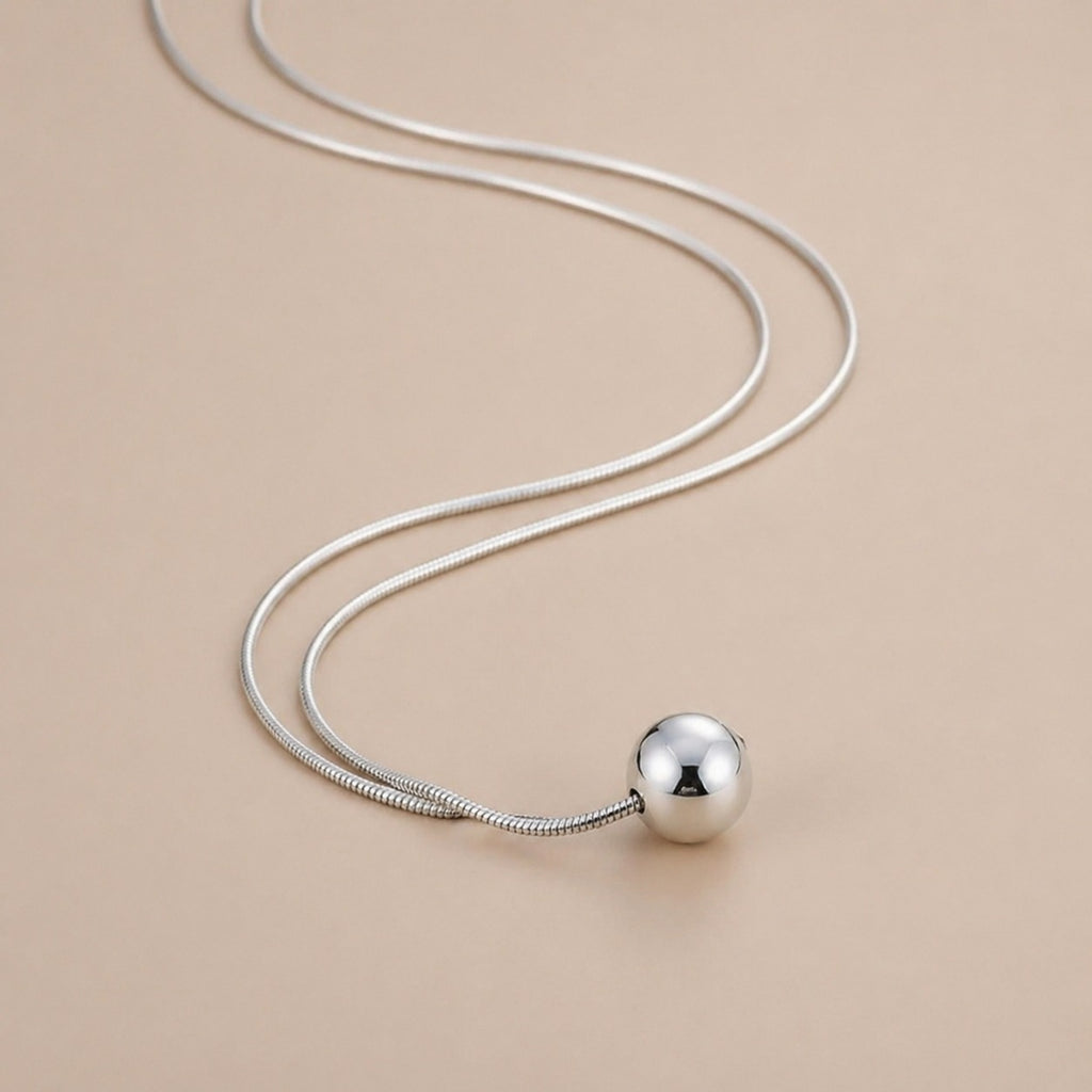 Sterling silver ball necklace on snake bone chain, minimalist boho jewelry with simple, elegant design.