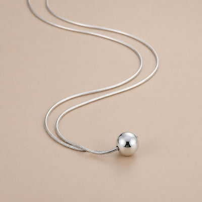 Sterling silver ball necklace on snake bone chain, minimalist boho jewelry with simple, elegant design.