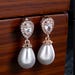 Load image into Gallery viewer, Teardrop pearl dangle earrings with crystal halo, elegant bridal jewelry by Luxe Treasures, showing the detailed design and sparkle.